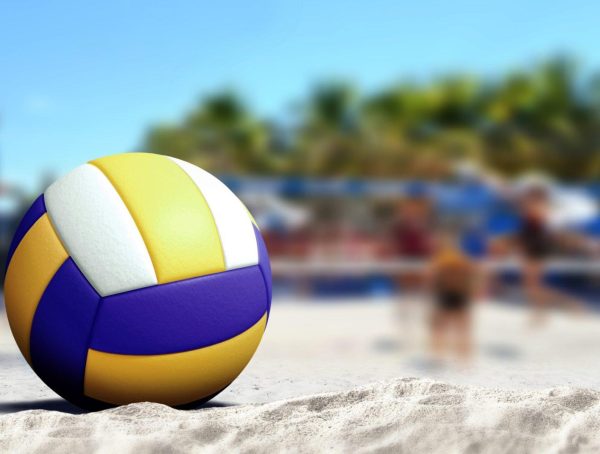 Volleyball ball on sandy beach with blur image of players playing in background